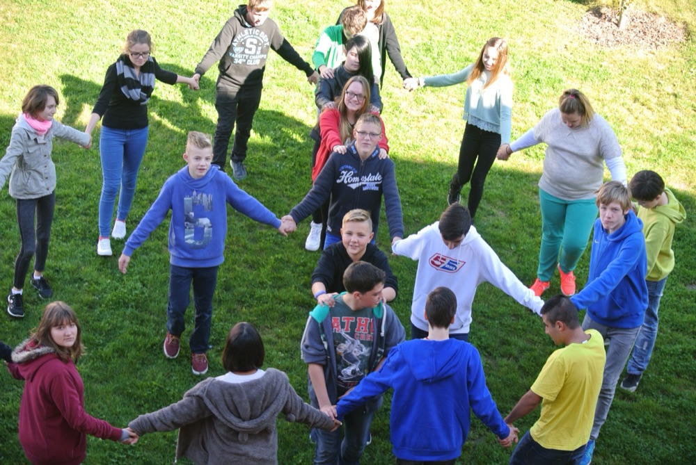 Schülerinnen und Schüler stehen Hand in Hand im Kreis auf der Wiese